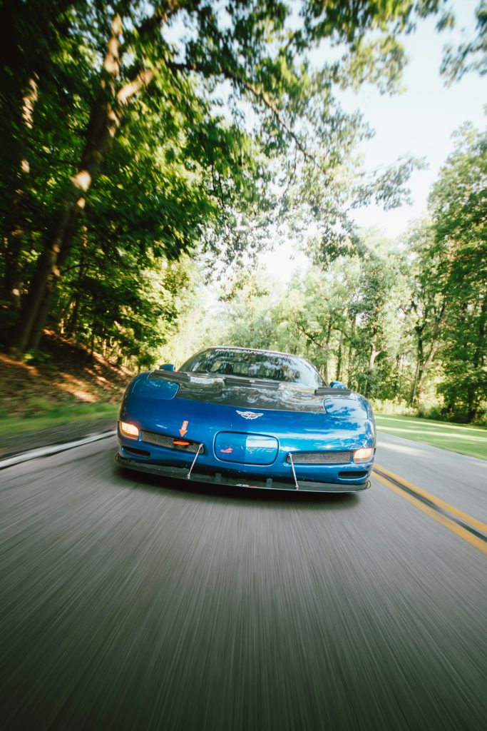 A blue sportscar driving towards the camera, framed by trees